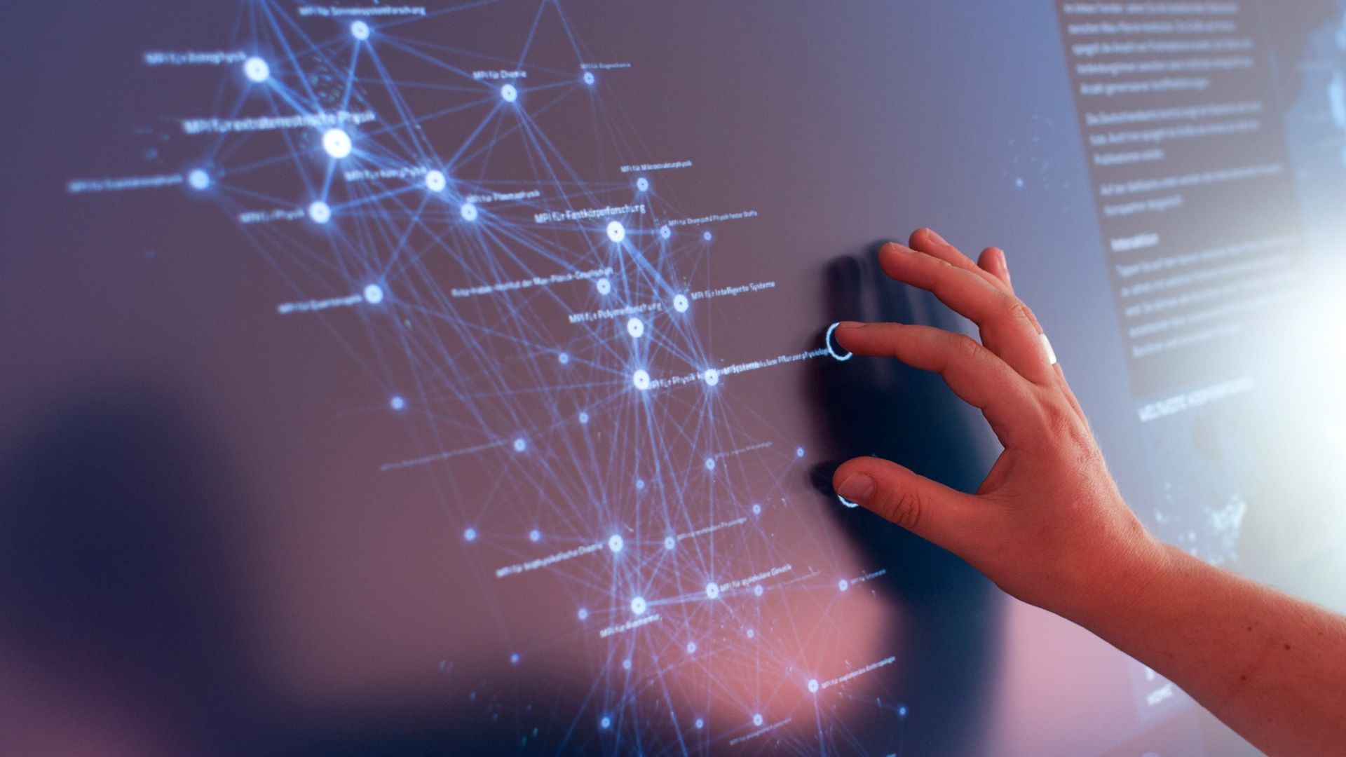 Hand touching a multitouch screen showing a glowing blue network of Max Planck Institutes