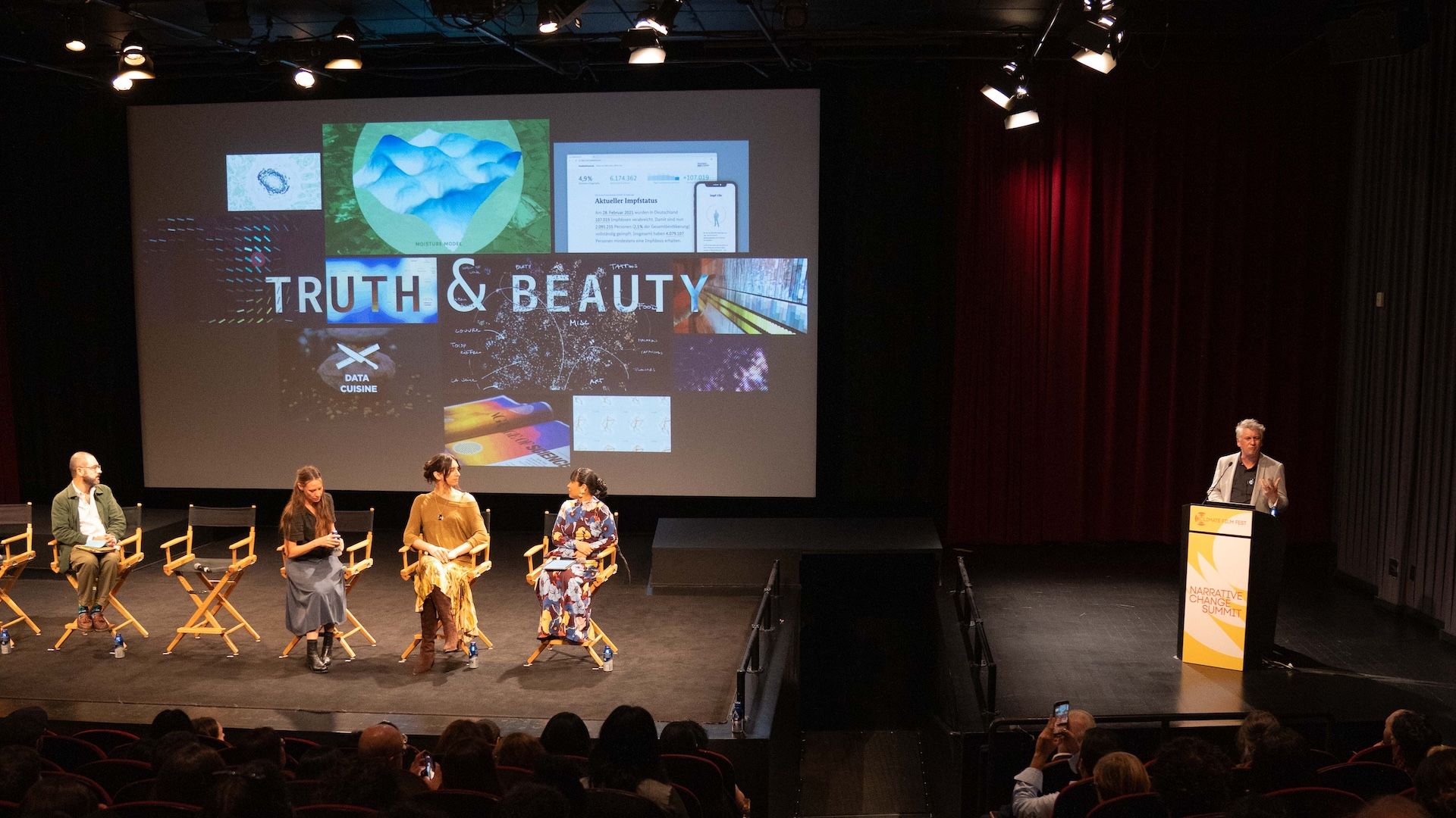 Moritz Stefaner presenting from the podium while panelists watch a projected Truth & Beauty collage of past projects