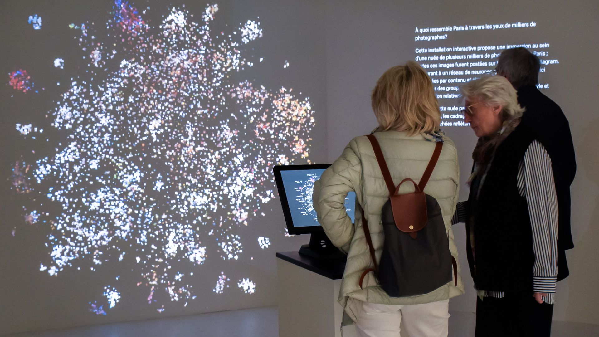 Visitors reading the French introduction beside the projected sparse photo cloud of the map overview