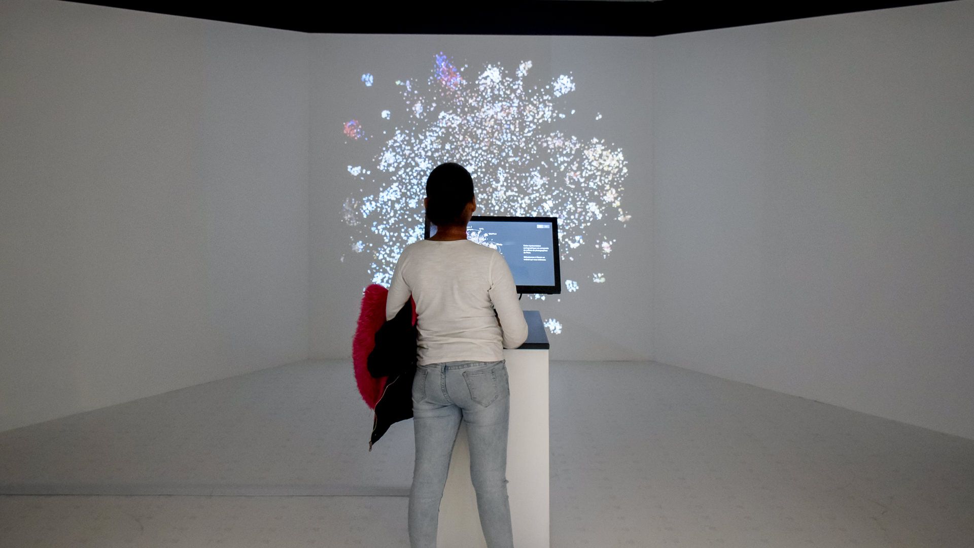 A visitor alone at the console facing the glowing photo cloud projected across the darkened room