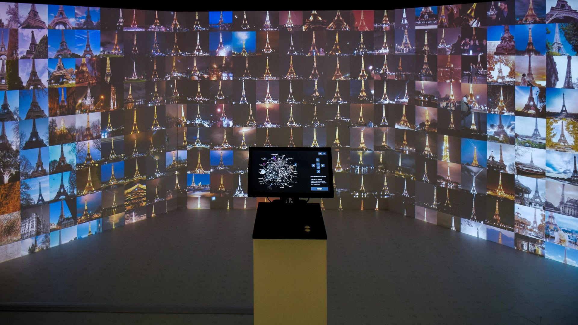 Installation view, projection wall filled with hundreds of Eiffel Tower photos around the touchscreen console
