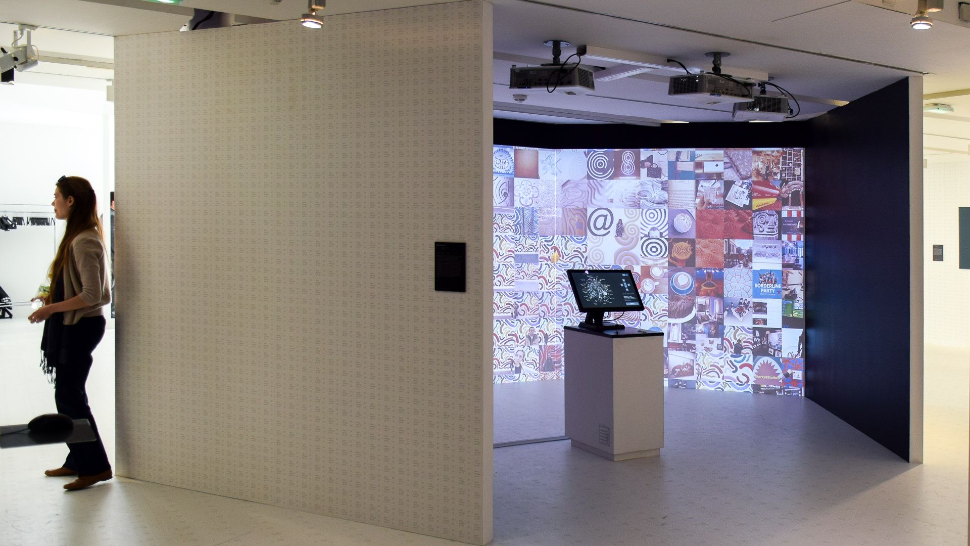 Gallery view of the installation booth with ceiling projectors and a visitor entering the projection room
