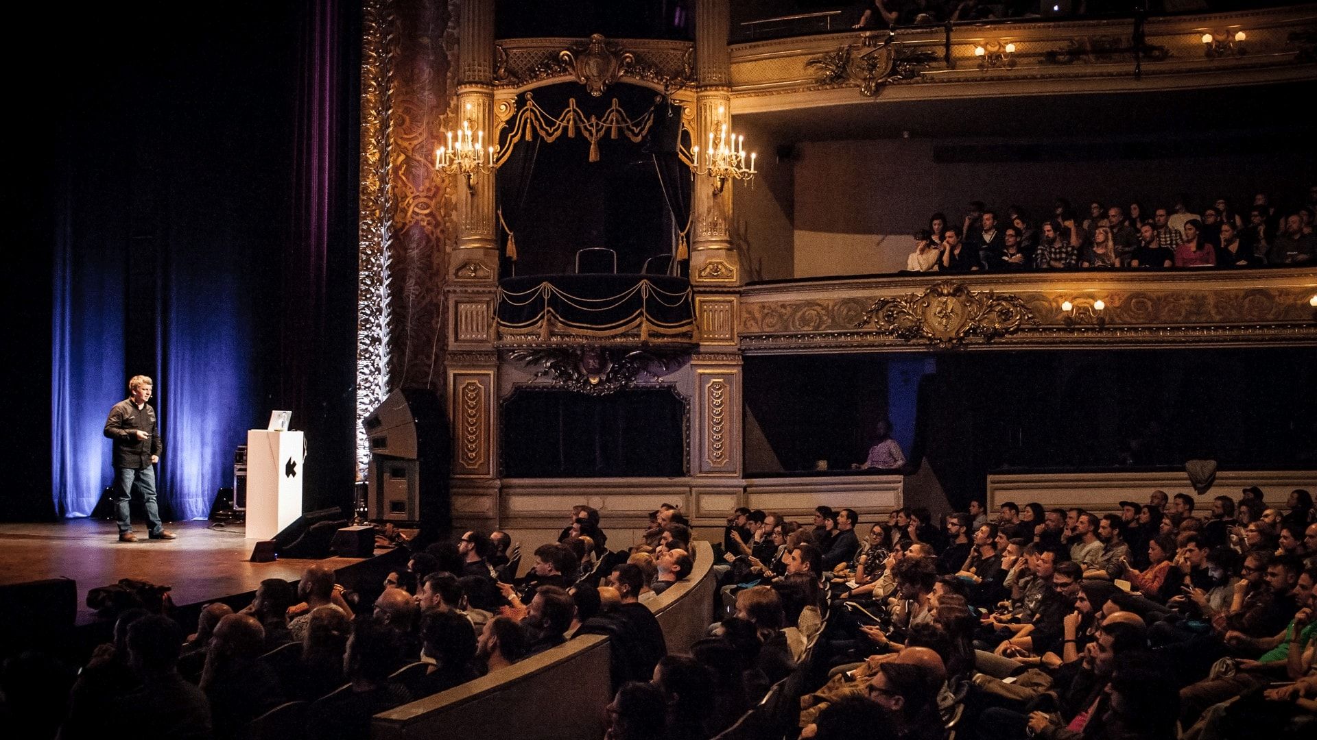 Moritz Stefaner speaking on stage in front of a large projected data visualization
